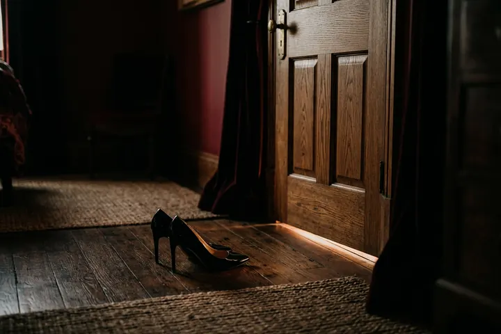 Porte close dans une pièce tamisée, un rai de lumière au sol et une paire d'escarpins en attente