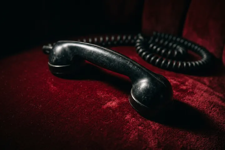 Combiné de téléphone noir posé sur un velours sombre, sous une lumière rasante
