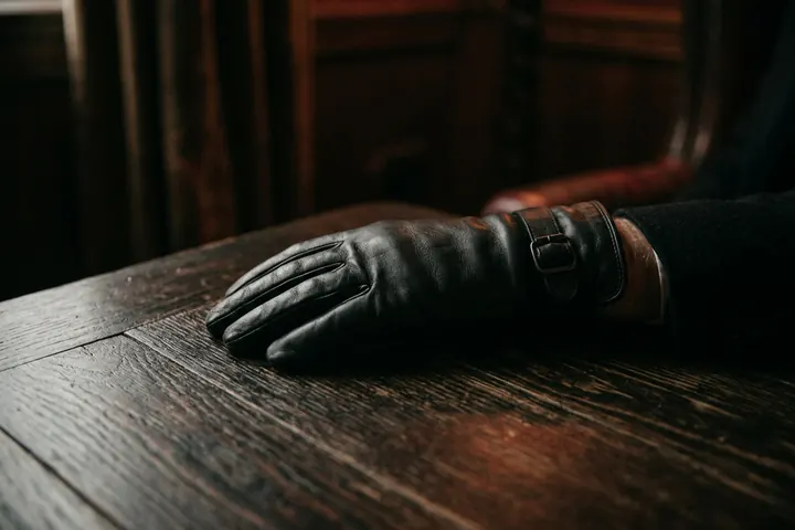 Gant de cuir noir posé sur une table en bois sombre, sous une lumière douce et rasante