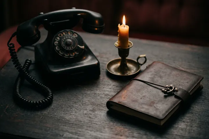 Téléphone ancien noir posé près d'une bougie allumée et d'un carnet en cuir fermé, dans une lumière chaude
